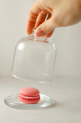 delicious delicate multi-colored macaroons on a platter. female hand closes a transparent glass lid on a light background. close-up. selective focus