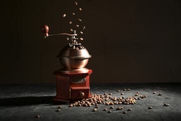 Wooden vintage coffee grinder on a slate plate, falling and lying roasted beans against a dark...