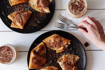 Woman's hand decorates the table with pancakes with chocolate, kiwi and banana. Black plate, white table. From above