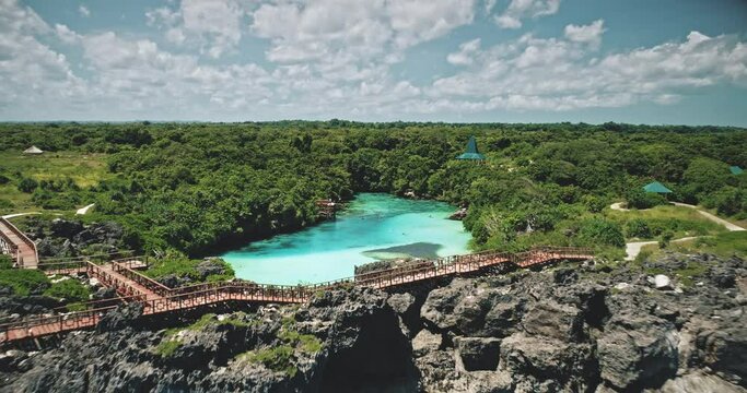 Green cliff ocean coast with limpid lake at tropic plants and trees in aerial view. Amazing nature landscape at Weekuri lake, Sumba Island, Indonesia, Asia. Greenery rocky sea shore at drone shot