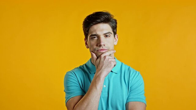 Thinking man looking up and around on yellow background. Worried contemplative face expressions. Handsome male model in blue t-shirt