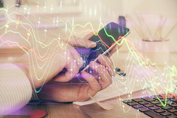Double exposure of man's hands holding and using a digital device and forex graph drawing. Financial market concept.