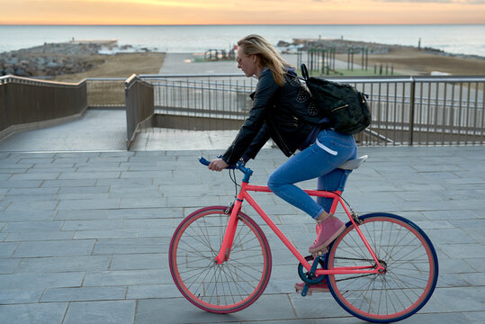Blonde woman riding bike against endless seascape at sunrise.