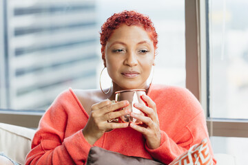 Black woman relaxing and drinking tea at home on couch