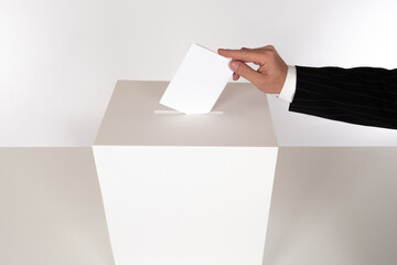 Man throws a ballot into voting box. Voter hand puts ballot in voting box. White ballot box on a...