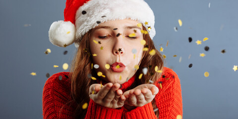 Beautiful woman is blowing confetti in the air, New Year party celebration. Isolated on gray background