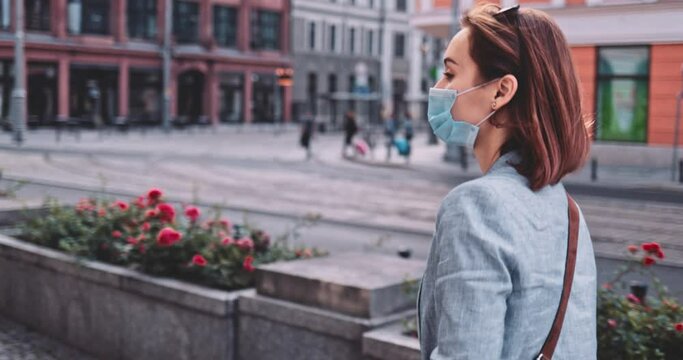 Woman Wearing A Protective Mask Walking In The City. SLOW MOTION, Gimbal Stabilizer. Young Female in face mask against air pollution and coronavirus Covid-19, out and about in street. Urban Morning. 