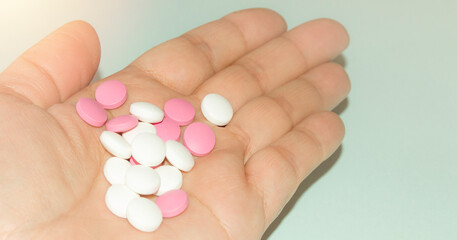 Open palm of a woman with a bunch of white and pink pills, health and medicine concept, close-up