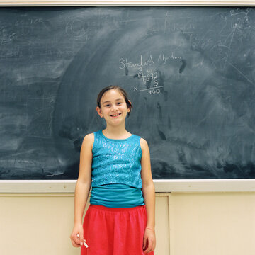 Eleven year old girl smiles in the middle of solving an equation on the classroom blackboard