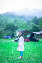 Fototapeta premium happy little asian girl in dress walking on the grass in front of tents while camping