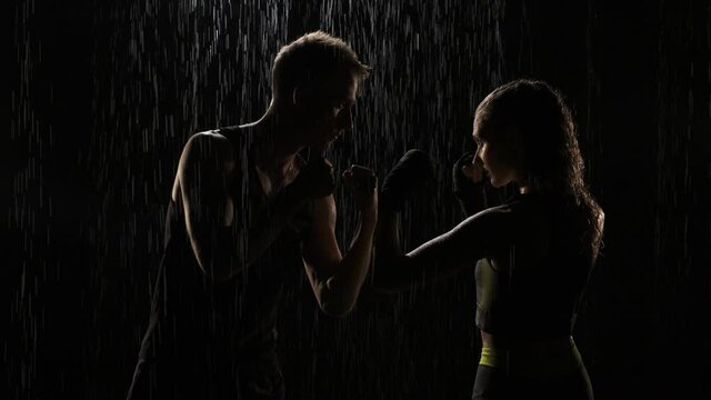Guy and girl stand in fight stand in the rain. woman and man are ready for fight and stand opposite each other. The girl is dressed in a gray-green top, guy is naked to the waist