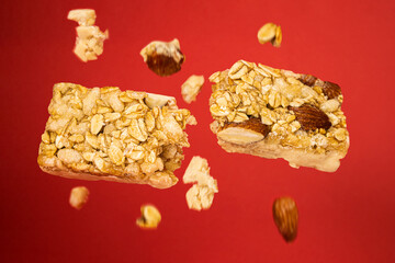 
granola bar broken in half floating on red phone with pieces of walnut oats grains cereals falling down healthy