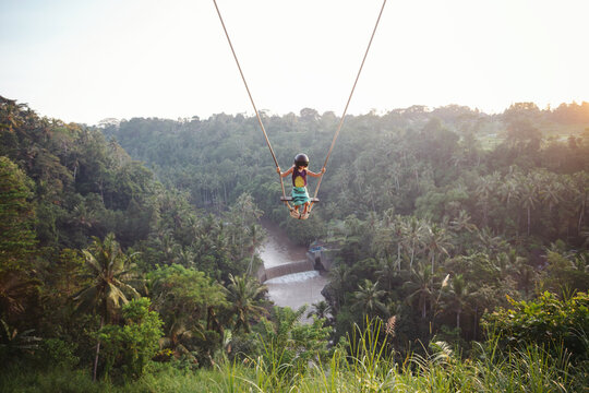 Brave young girl on hgh swing at sunrise