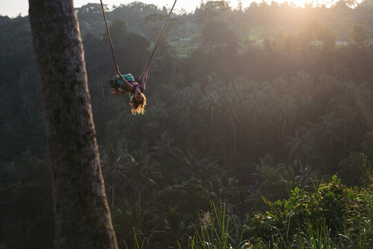 Brave young girl on hgh swing at sunrise