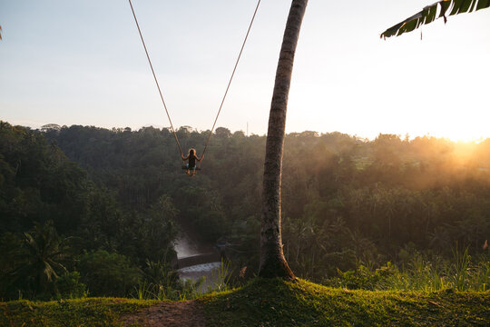 Brave young girl on hgh swing at sunrise