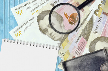 100 Ukrainian hryvnias bills and magnifying glass with black purse and notepad. Concept of...