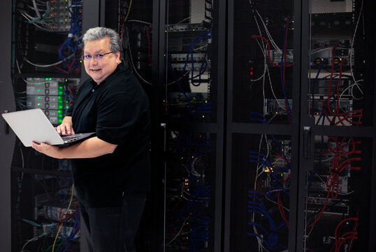 Hispanic male computer expert in server room holding laptop