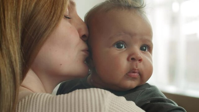 Close up of Caucasian woman holding cute mixed-race baby girl in her hands and kissing her in cheekbone