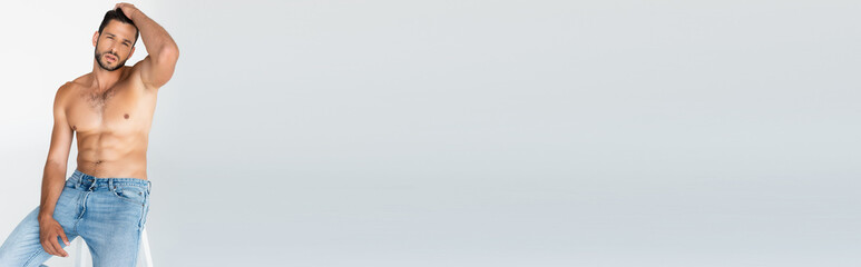 Fototapeta premium panoramic crop of shirtless and bearded man sitting and touching hair on grey