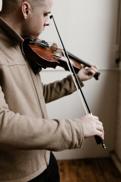stylish young man standing and playing the violin in a studio