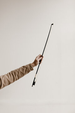 arm holding out violin bow against a white studio wall