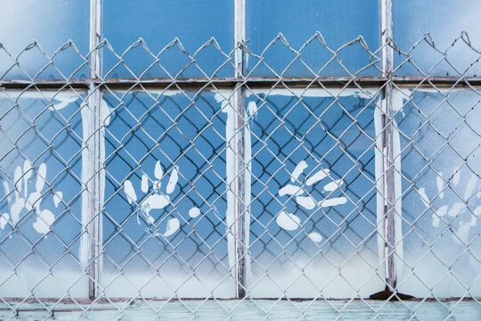 White paint handprints on window behind wire mesh fence