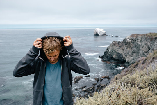 Man pulls up his hood on his sweater as the wind picks up and it gets colder