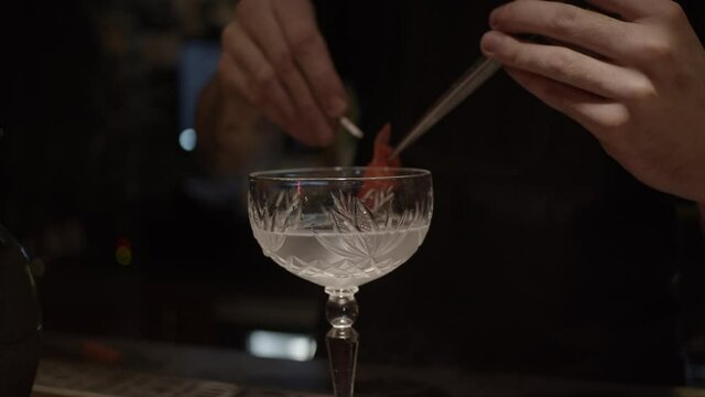 Attaching marinated ginger as decoration on glass with sake based cocktail, slow motion