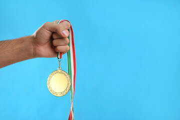 Fototapeta na wymiar Man holding golden medal on light blue background, closeup. Space for design