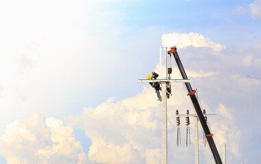 Fototapeta premium A male worker wearing safety equipment (yellow helmets, safety shoes, and seat belt) is working on installing equipment for power lines on high-voltage towers. Using a crane to transport equipment.