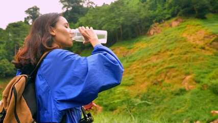 Young woman backpacker hasing water break whlie exploring the nature.