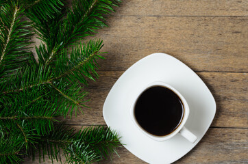 Fir branches with green needles, Christmas balls and a Cup of coffee on a saucer on a wooden background.