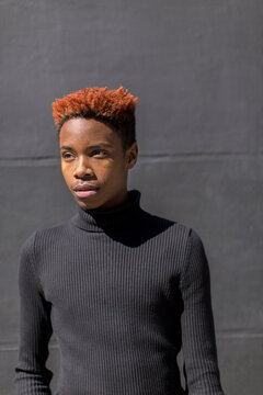 Young black man standing against a black wall.