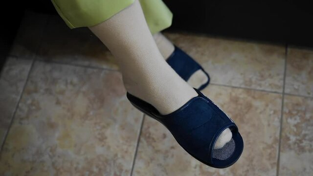 A girl with in blue slippers sits on the couch and shakes her leg. Close-up foot