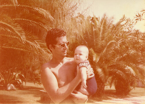 Man in sunglasses with son against palm trees.