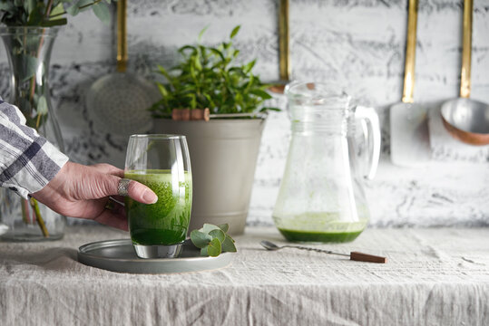 Female hand reaching for a green juice drink from a table.