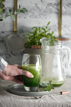 Female hand reaching for a green detox smoothie drink from a table.