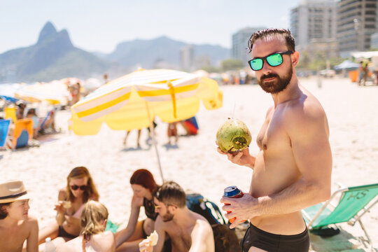 Man in bathing suit holds coconut on beach