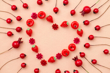 Miniature decorative fruits and red berries arranged in a heart shape on felt fabric with a top view