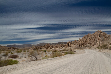 Adventure. Driving along the dirt road across the arid desert. The route, rocky valley and sandstone hills under a beautiful blue sky.