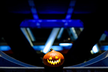 Halloween pumpkin in the dark on a blue industrial abstract background. Blurry colored lights. The decor of the night city in a festive Halloween theme. Copy space.