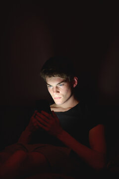 Young man resting on a couch using his phone in the dark