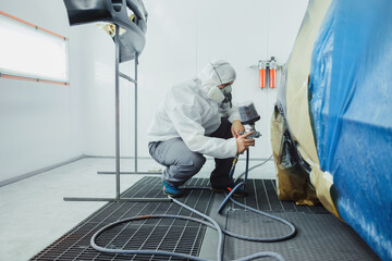 Worker/painter working on car bodywork in paint chamber/workshop.