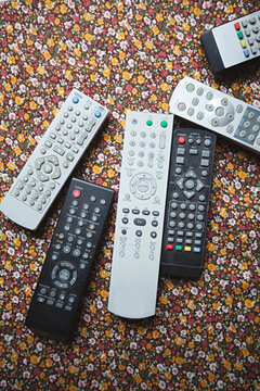 Collection of old television, dvd, video remote controls on flower table cloth