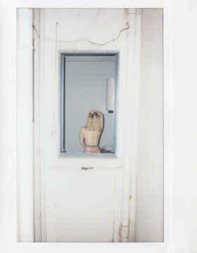Topless woman in tights through window frame.