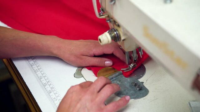 Closeup of female hands with manicure working on a sewing machine.