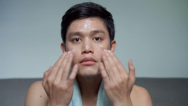 Close Up Young Asian Man Applying Sunscreen Uv-protection On Face And Smile While Thinking And Looking On Grey Background For Advertising Product Concept	