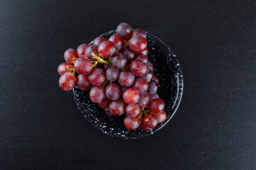 Red grapes in a bowl on dark grey background, flat lay.