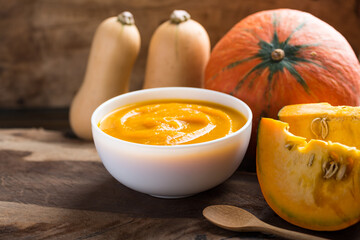 Pumpkin soup in a bowl and fresh pumpkins on wooden background