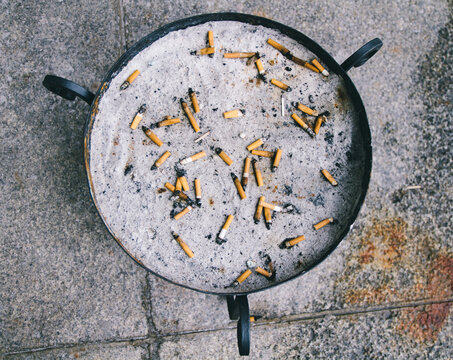Circular metal ashtray with sand and cigarettes